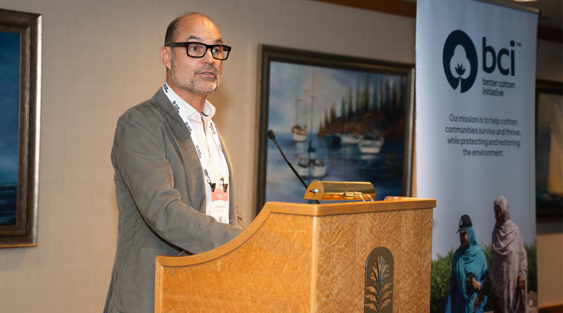 A speaker presenting beside a Better Cotton Initiative banner.